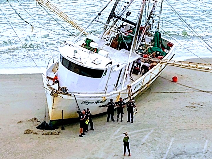 The Shayne Michelle on the sand seen from above, officers standing alongside her bow