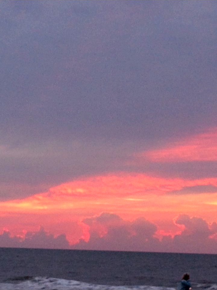 A purple dawn sky over the ocean, bands of pink and orange light glowing above dark clouds on the horizon