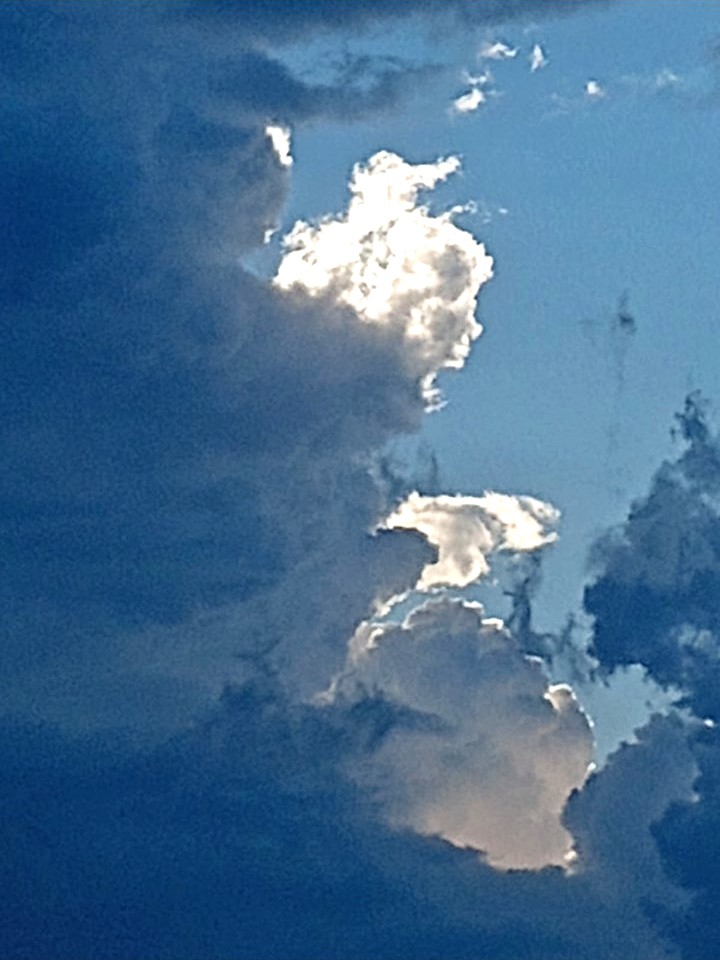 Sunlit white clouds edged in light against a deep blue sky, a bright cloud formation standing out from the shadowed clouds around it