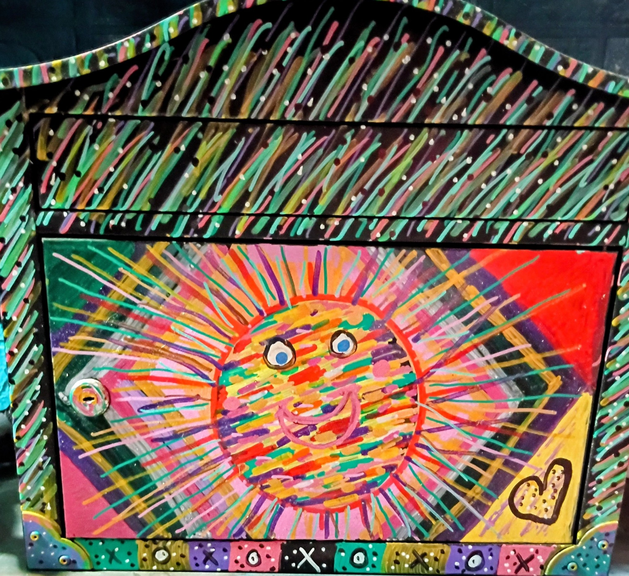 Mia Roze Bootz's hand-painted mailbox — a smiling rainbow sun on the door, multicolour rays streaking across the top, and an XOXO border along the bottom