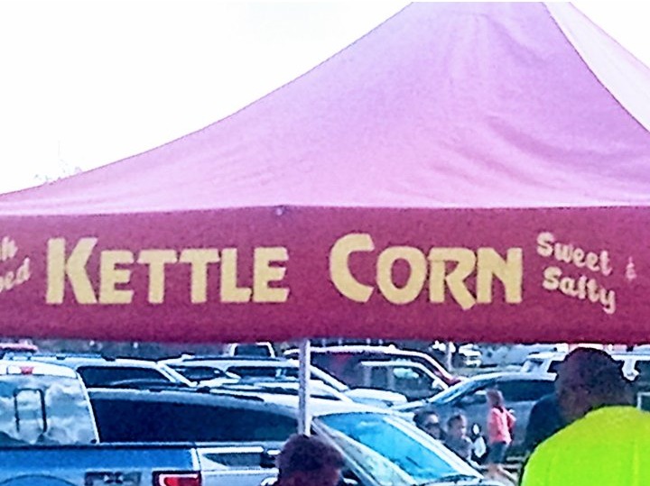A red Kettle Corn tent banner lettered Sweet and Salty in cream, over a busy parking lot