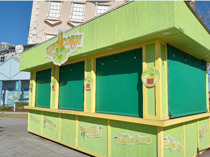 The King Corn stand — a bright green and yellow boardwalk stand signed King Corn, Roasted Corn, and Fresh Lemonade, its green shutters closed
